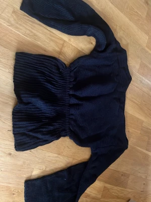 Svart stickad tröja med vida ärmar - Trendig svart stickad tröja med markerad midja och vida, långa ärmar. Tröjan har en lös passform nedtill och är tillverkad i mjukt stickat material. Perfekt för dig som gillar en avslappnad men ändå stilsäker look.