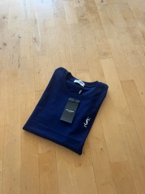 Mörkblå YSL t-shirt med logga - Snygg mörkblå t-shirt från Saint Laurent med klassisk vit YSL-logga broderad på bröstet. T-shirten har rund hals och korta ärmar, perfekt för en clean och stilren look. Tillverkad i mjuk bomull för skön komfort.