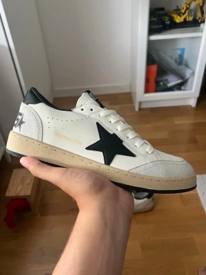 Golden Goose ballstar sneakers  - Snygga vita sneakers från Golden Goose med svart stjärndetalj på sidan, svart häl och beige sula. Skorna har GGDB Ballstar-tryck i guld, perforerade detaljer och vita skosnören. skorna är super rena och knappt använda, st 43 men kan oxå passa 44