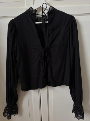 HM blus - Svart blus med fina spetsdetaljer. Blusen är öppen i ryggen med knytdetaljer. Lite liten i storlek🤍