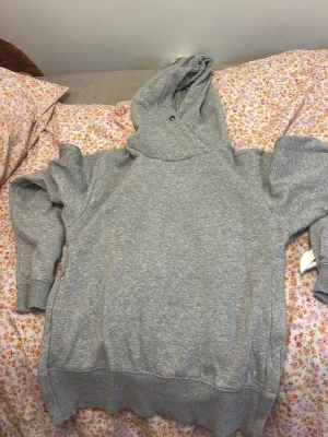 Grå hoodie med huva - En klassisk grå hoodie i mjukt sweatshirtmaterial. Hoodien har en stor huva med dragsko och ribbade muddar vid ärmslut och nederkant. Perfekt för en avslappnad och chill stil.