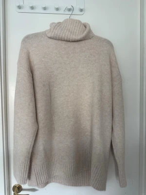 Beige polotröja i mjuk stickning - Säljer en oversized beige stickad polotröja med bred ribbstickning vid ärmslut och nederkant. Tröjan har en hög, vikt polokrage och är gjord i ett mjukt material. Från Nakd, säljes då den inte använts. Lappen är kvar! 
