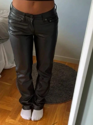 Svarta skinnbyxor med raka ben - Snygga svarta skinnbyxor med raka ben och klassisk femficksdesign. Byxorna har hög midja och stilren look som passar till många olika outfits. Materialet är glansigt skinn som ger en cool vibe.