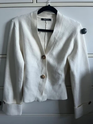 Gina tricot topp med knappar - Stilren vit tröja från Gina Tricot med två dekorativa knappar framtill och uppvikta ärmslut. Rak passform och mjukt tyg som ger en avslappnad men ändå chic look. Perfekt att matcha med jeans eller kjol för en trendig outfit.