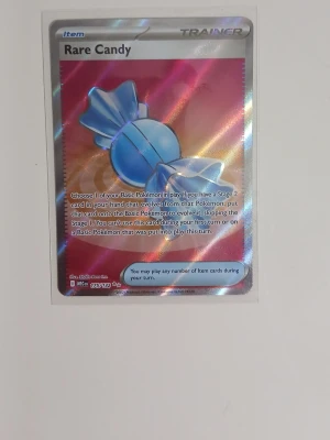 Pokémonkort Rare Candy holo - Säljer ett Pokémonkort av typen Trainer Item: Rare Candy. Kortet har en holografisk yta med en blå godis-ikon mot en skimrande bakgrund. Text och detaljer är på engelska. Perfekt för samlare eller Pokémon TCG-spelare.