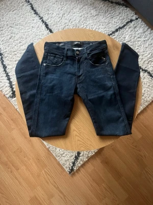 Mörkblå Replay Anbass - Tjena👋 Säljer dessa snygga mörkblå Replay i slim fit-modell med klassisk femficksdesign och silverfärgade nitar, i storlek W28 L34 i Anbass modell😮‍💨 Jeansen har normal midja och raka ben😎Materialet är denim med lätt stretch för extra komfort🤩 Perfekta till en avslappnad och trendig stil🧼 Meddela gärna vid frågor!📩