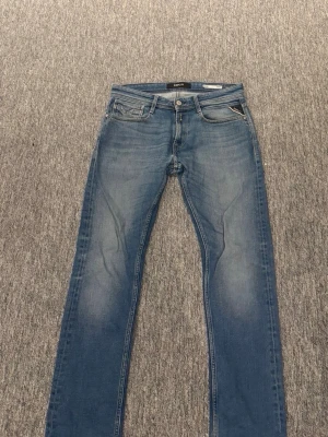Blå slim fit jeans från Replay - Snygga blå slim fit jeans från Replay med klassisk femficksdesign och diskreta slitningar. Jeansen har normal midja och dragkedja med knapp. Perfekta för en avslappnad och trendig look. Nypris 900kr