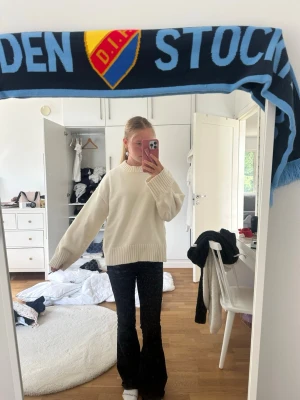 Vit oversized stickad tröja - Säljer en vit oversized stickad tröja med bred ribbad mudd vid hals, ärmslut och nederkant. Tröjan har en avslappnad passform och är perfekt för lager på lager. Materialet ser mjukt och mysigt ut, perfekt för kyligare dagar.