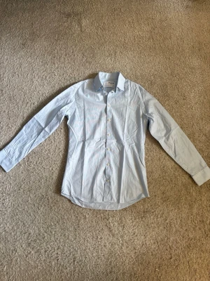Selected Homme Slim skjorta - Stilren ljusblå skjorta från Selected Homme i slim fit. Perfekt både till jobb, fest och vardag. Sparsamt använd och i mycket fint skick.  📦 Snabb leverans! 💬 Skicka gärna ett meddelande om du vill ha fler bilder eller mått.