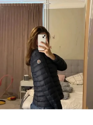 Svart dunjacka från Moncler - Snygg svart dunjacka från Moncler med quiltad design och hög krage. Jackan har dragkedja framtill och Moncler-logga på ärmen. Perfekt för kalla vinterdagar och ger en stilren look. Nypris ca 7000 då de e i barn storlek, 14 år.