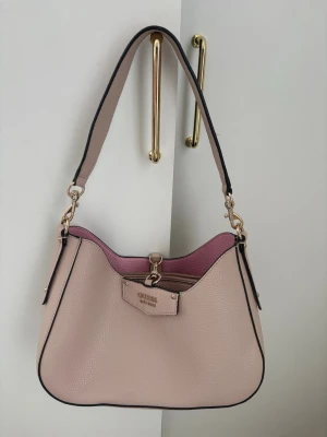 GUESS VÄSKA  - Väska från guess i nyskick. Ljusrosa med mörkare rosa insida. Medföljer necessär. Ny pris 1200kr. Mått: Höjd 17, Bredd 28, Djup 8. 