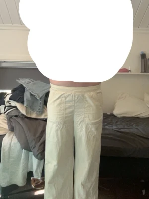 Vida beige linnebyxor med fickor - Säljer ett par ljusbeige linnebyxor med raka, vida ben och stora utanpåfickor framtill. Byxorna har hög midja och avslappnad passform, perfekta för en chill och stilren look. Materialet är tunt och luftigt, vilket gör dem sköna att bära under varma dagar.