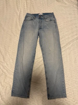 Ljusblå raka jeans - Säljer ett par ljusblå jeans med rak passform och klassisk femficksdesign. Jeansen har normal midja och är tillverkade i denim med en snygg tvättad look. Perfekta till en avslappnad stil och passar till det mesta i garderoben.