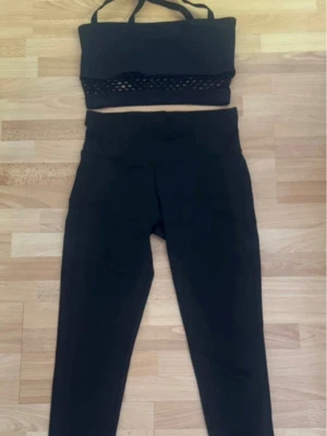 Svart träningsset med meshdetalj - Snyggt svart träningsset med sport-bh och höga tights. Sport-bhn har coola meshdetaljer nedtill och smala axelband. Tightsen är höga i midjan och sitter tajt. Perfekt för gymmet eller yoga. Behå är från Better Bodies, leggings vet ej.