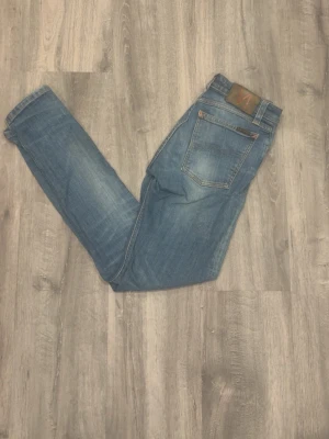 Nudie  - Säljer ett par klassiska blå jeans från Nudie  med smal passform och fem fickor. Jeansen har en snygg tvättad look. Perfekta för dig som gillar en enkel och stilren stil.