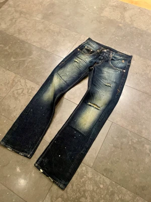 Jeans Archive Distressed Faded Bootcut Washed - 📏 Storlek: [30/32] 🎨 Färg: [Mörk blå med grön/vit fades] 👖 Modell/passform: [Straight / Bootcut] 📐 Midjemått: [38 cm] 📏 Innerbenslängd: [80cm] 📏 Benöppning: [21cm] 👨‍🎨 Modellen på bilden är 183cm lång och väger 63kg ✨ Skick: [Mycket bra] 📝 Beskrivning: Snygga jeans i fint skick, sparsamt använda.  ⚠️ Eventuella fel/slitage: [Kan vara lite hårda i tyget]  📦 Skickas snabbt och packas noggrant! 💬 Hör gärna av dig om du har frågor eller vill ha fler bilder.   