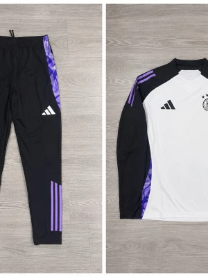 Adidas Tyskland träningsset svart/vit - Snyggt träningsset från Adidas med Tysklands landslagslogga. Tröjan är vit med svarta ärmar och lila detaljer på axlarna. Byxorna är svarta med lila mönstrade ränder längs sidorna och Adidas-logga. Perfekt för fotbollsträning eller gymmet.
