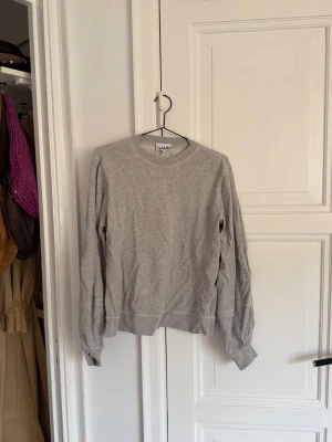 Ganni - Grå sweatshirt - En stilren grå sweatshirt från Ganni med rund halsringning och långa ärmar. Tröjan har en avslappnad passform och ribbade muddar vid ärmslut och nederkant. Perfekt för en casual look och enkel att matcha med olika outfits.