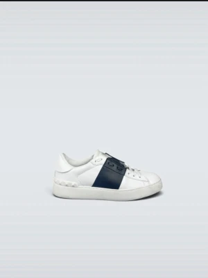 Vita sneakers med svart detalj - Snygga vita sneakers med en bred svart rem över snörningen. Skorna har en klassisk låg profil och är tillverkade i slätt läder. Sulan är vit och har nitar längs kanten för en extra touch. Perfekta för dig som gillar stilrena och moderna sneakers.