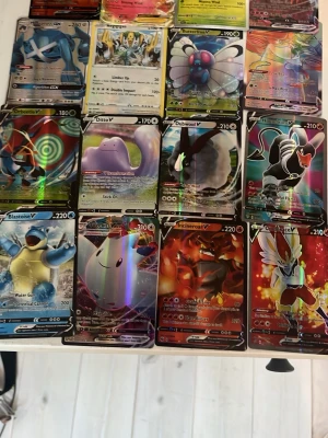 Samling Pokémonkort V och GX - Stor samling Pokémonkort med flera V, GX och holografiska kort. Blandade motiv som Blastoise, Ditto, Incineroar och Butterfree. Flera kort har färgstarka illustrationer och glansig finish. Perfekt för dig som vill utöka din samling eller byta med vänner.