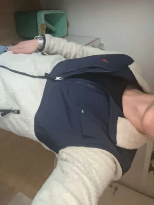 Teddyjacka från Polo Ralph Lauren - Säljer en snygg teddyjacka från Polo Ralph Lauren i beige och marinblått. Jackan har dragkedja framtill, två sidofickor med dragkedja och en bröstficka med knapp. Mysigt teddy-material och klassisk logga på bröstet. Den är j jättefint skick med inga defekter alls!