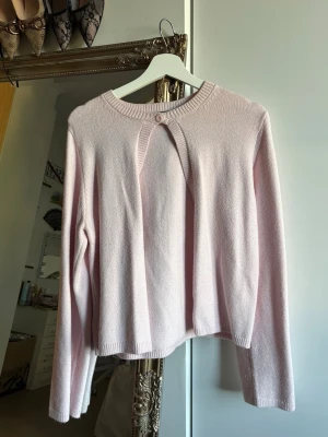 Ljusrosa stickad cardigan med knappdetalj - Supersöt ljusrosa stickad tröja med lång ärm och en unik knappdetalj vid halsringningen. Använd en gång. Väldigt trendig, från gina