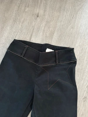 Low waist byxor med stjärndetalj  - Unik vintage-stjärna med edge! Dessa byxor har en dekorativ stjärna i kontrastsöm, bälteshällor och nitar längs kanten för extra karaktär.  ✨ Äkta 90-talsvintage från mammas garderob, i mycket bra skick med dragkedja i midjan. Lågmidjiga och utsvängda för en bekväm, tidlös look.  📏 Midja 37 cm (Lapp säger M men jag skulle säga mer av S), innerbenslängd 78 cm.  Perfekta för dig som vill sticka ut med vintage-charm och personlig stil! 💫✨