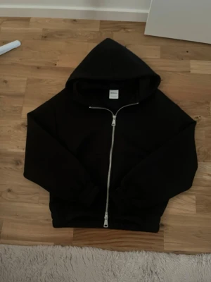 Svart zip hoodie från Bershka - Säljer en svart hoodie från Bershka i storlek XS. Hoodien har dragkedja framtill, stor huva och ribbade muddar vid ärmslut och nederkant. Perfekt för en chill och avslappnad stil. Materialet känns mjukt och bekvämt.