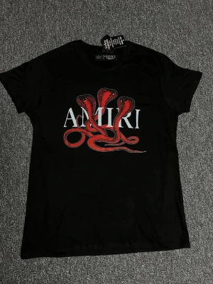AMIRI svart T-shirt med rött ormtryck - Svart T-shirt med stort AMIRI-tryck och röda ormar framtill. Snygg och unik streetwear-design med bekväm passform. I mycket fint skick.