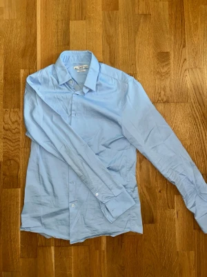 Ljusblå skjorta från MNG - Säljer en ljusblå skjorta från MNG med super slim fit. Skjortan har klassisk krage, långa ärmar och knappar framtill. Perfekt för dig som gillar en stilren och enkel look.