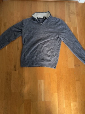 Grå quarter zip tröja med ståkrage - Snygg grå tröja med halvzip och ståkrage. Insidan av kragen är vit och ger en schysst kontrast. Tröjan har långa ärmar och är tillverkad i ett mjukt, tunt material som passar perfekt till lager på lager. Enkel och stilren design som funkar till det mesta.
