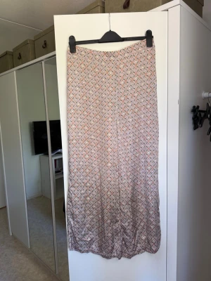 Mönstrad byxor  i pastellfärger - Säljer en flowy byxor med ett småmönstrat tryck i ljusa pastellfärger som rosa, beige och lite grönt. Kjolen har en rak passform och är gjord i ett tunt, mjukt material som känns skönt mot huden. Perfekt för vår och sommar! Från märket Odd Molly i storlek 3 som enligt deras storlekguide motsvarar en storlek L. Kanske något små i storlek. Mycket fint skick, jag hittar inga synliga anmärkningar eller defekter. 