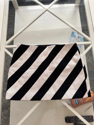 Svartvit kortkjol med diagonala ränder - Säljer en snygg kortkjol med svartvita diagonala ränder. Kjolen har en rak passform och är tillverkad i ett tjockare tyg som ger struktur. Perfekt för dig som vill sticka ut med ett grafiskt mönster.
