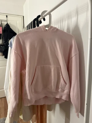 Ljusrosa hoodie från 157  - Säljer en ljusrosa hoodie från 157 i storlek XS. Hoodien har en klassisk huva och en stor magficka framtill. Tillverkad i mjukt bomullsmaterial och har ribbade muddar vid ärmslut och nederkant. 