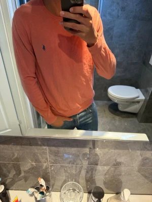 Korallfärgad tröja från Ralph Lauren - Snygg långärmad tröja i korall från Ralph Lauren med den klassiska broderade loggan på bröstet. Tröjan har rund halsringning och är tillverkad i ett mjukt, tunt material som passar perfekt till jeans.jag på bilden är 188cm. Tröjan är i riktigt bra skick och har inga skador. Hör av er vid eventuella funderingar;)