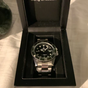 Kompass OceanXplorer Silver Green Black - Snygg Kompass OceanXplorer klocka med robust silverfärgad länk i metall, svart urtavla och grön bezel. Klockan har tydliga index, datumvisning och quartz-urverk. Perfekt för dig som gillar stilren design med sportig känsla.