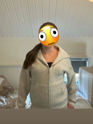 Ljusgrå zip hoodie med huva - En stilren ljusgrå hoodie med dragkedja framtill och stor huva. Tillverkad i mjukt sweatshirtmaterial och har två fickor framtill. Perfekt för en avslappnad och bekväm look. Den sitter mer som en S!