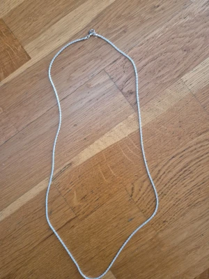 Silverfärgat kedjehalsband - Säljer ett stilrent silverfärgat halsband med tunn kedja. Halsbandet har en enkel karbinhake och mäter cirka 60 cm långt. Perfekt för dig som gillar minimalistiska smycken och vill ha något som passar till många olika stilar.