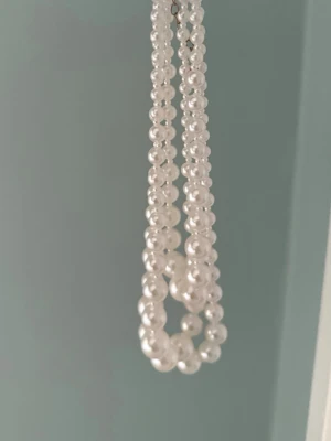 Vitt pärlhalsband i flera rader - Säljer ett snyggt halsband med flera rader vita pärlor. Halsbandet har en klassisk design med runda pärlor i olika storlekar och ett metallspänne. Perfekt för dig som vill ha en elegant accessoar som sticker ut.