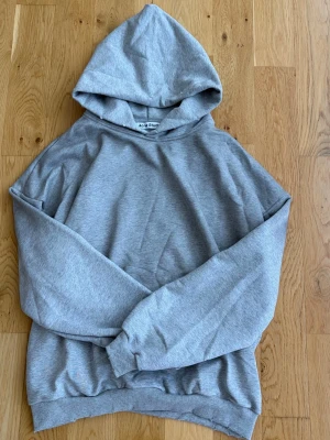 Grå hoodie från Acne Studios - Snygg grå hoodie från Acne Studios med tryck på ryggen där det står 'Acne Studios STOCKHOLM 1996'. Klassisk passform med huva och ribbade muddar vid ärmslut och nederkant. Perfekt för en avslappnad och trendig look.