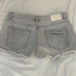 Grå jeansshorts med slitningar - Snygga Lågmidjade grå jeansshorts med slitna detaljer och fransig kant. Säljer då de inte passade mig