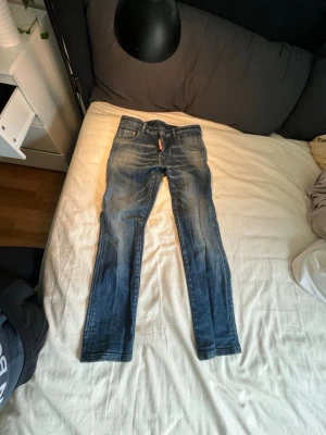 Blå jeans från DSQUARED2 - Säljer ett par blå smala jeans från DSQUARED2 med slitningar och tvättade detaljer. Klassisk femficksmodell med knappgylf och snygg passform. Tillverkade i bomull med en cool vintage-look.