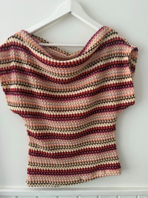 Randig virkad topp i rosa och beige - Unik virkad topp med bred halsringning och korta ärmar. Toppen har ett randigt mönster i rosa, vinrött, beige och brunt. Perfekt för dig som gillar boho-vibbar och vill sticka ut med färg och struktur. Sitter löst och är superbekväm till jeans eller kjol.