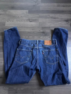 Mörkblå jeans  - Säljer ett par klassiska mörkblå jeans från levis med raka ben och knappgylf. Jeansen har fem fickor, kontrastsömmar och bälteshällor. Passar perfekt till en avslappnad stil och är tillverkade i slitstark denim.