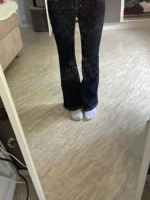 Mörkblå bootcut jeans med kontrastsömmar - Säljer ett par mörkblå bootcut jeans med vita kontrastsömmar och klassiska bakfickor. Jeansen har låg midja och är tillverkade i ett denimtyg som sitter snyggt på benen. Perfekta för dig som gillar en tidlös och trendig look.