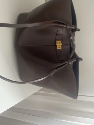 Mörkbrun gina väska i skinn helt ny - Stilren och rymlig shoppingväska i mörkbrunt skinn med långa axelband och guldfärgat spänne framtill. Väskan har en mjuk, slouchy form och minimalistisk design som gör den enkel att matcha med olika outfits. Perfekt för dig som vill ha plats för allt du behöver under dagen. Passar höstens mode perfekt 👌🏼 