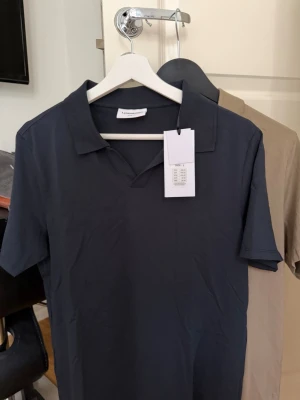 Mörkblå och beige piké t-shirt - Två stilrena piké t-shirts i mörkblått och beige. Från LINDBERGH, En är helt oanvänd med prislapp kvar, den beigea är använd en gång!!!                         Ordinarie pris: 499kr st, jag säljer båda för 499kr