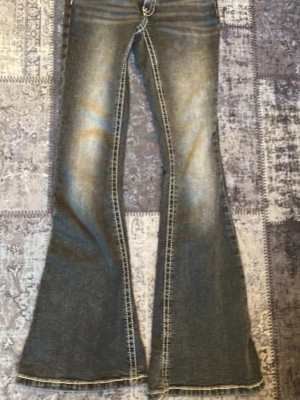 Blå bootcut jeans med slitningar - Endast upphämtning ❤️ Säljer ett par blå bootcut jeans med tydliga slitningar och kontrastsömmar. Jeansen har utsvängda ben och klassisk femficksdesign. Materialet är denim i bomull och passformen är relaxed med markerade sömmar längs benen.