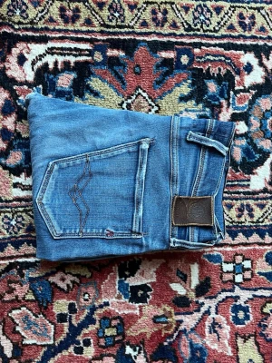 Replay anbass - Replay Anbass jeans i storlek W30 / L32 Säljer dessa snygga Replay Anbass-jeans. Klassisk slim/skinny-modell med den där lite slitna, coola looken som är typisk för märket. Jeansen har en fin, medelblå tvätt med diskreta slitningar och en tydlig reva på ena låret. Frickade fickor och lite fransar ger den där autentiska denim-känslan. Jag är 175 cm lång och väger 70 kg – de sitter snyggt och ganska tight på mig (se bilderna). Midja 30, benlängd 32. Skick: Använda men i fint skick, inga stora defe