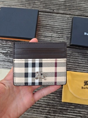 Burberry rutigt kortfodral - Säljer ett stilrent kortfodral från Burberry i klassiskt beige, svart och rött rutmönster med bruna detaljer. Tillverkad i canvas och läder, med Burberry-logga i metall framtill. Perfekt för kort och ID. Kommer med original ask, tygpåse och kort. Aldrig använd